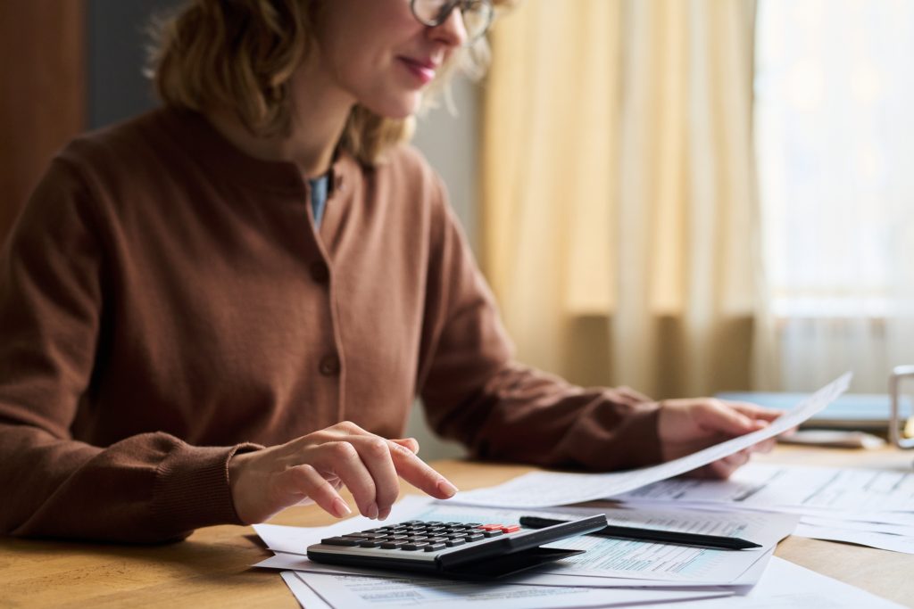 Midsection of young female specialist using calculator while sitting at desk in office and planning budget